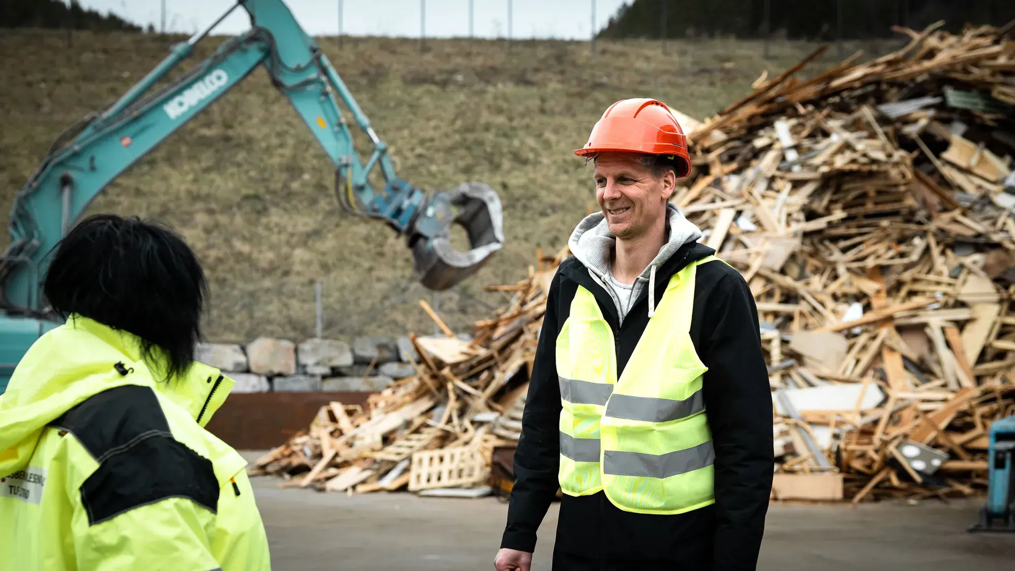 Christian Natadal fra PK Eiendom i samtale på anlegget til Kongsberg Samlesentral, med gravemaskin og trevirke i bakgrunnen