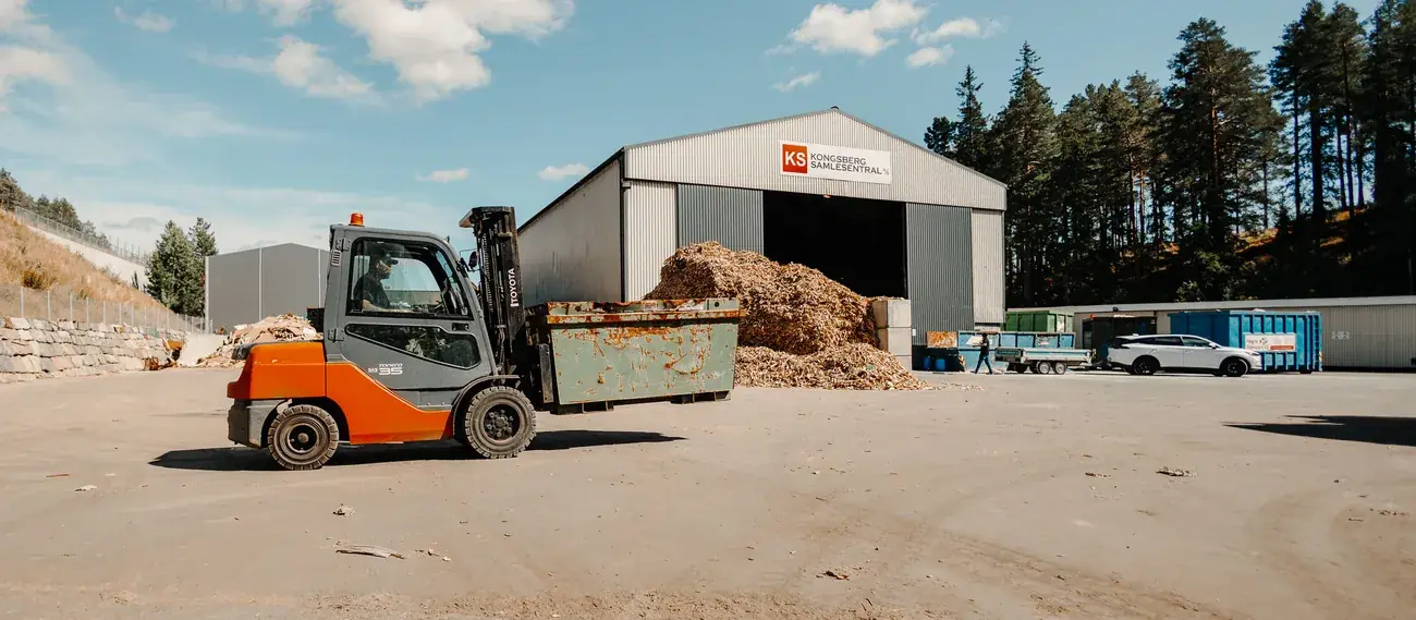Anlegget på Moane en sommerdag: hallen med KS-skiltet, en truck med container og flishauger