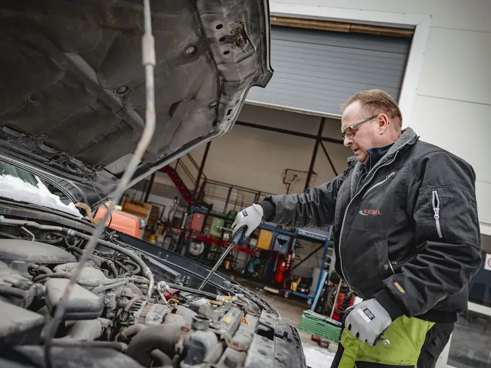 Ansatt tapper væsker fra motorrommet på en bil under miljøsanering