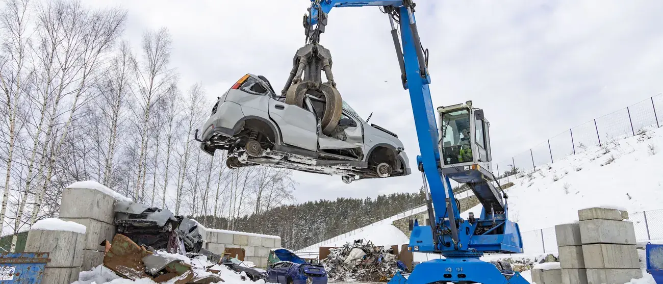 Materialhåndterer løfter en vrakbil med gripeklo på anlegget på Moane