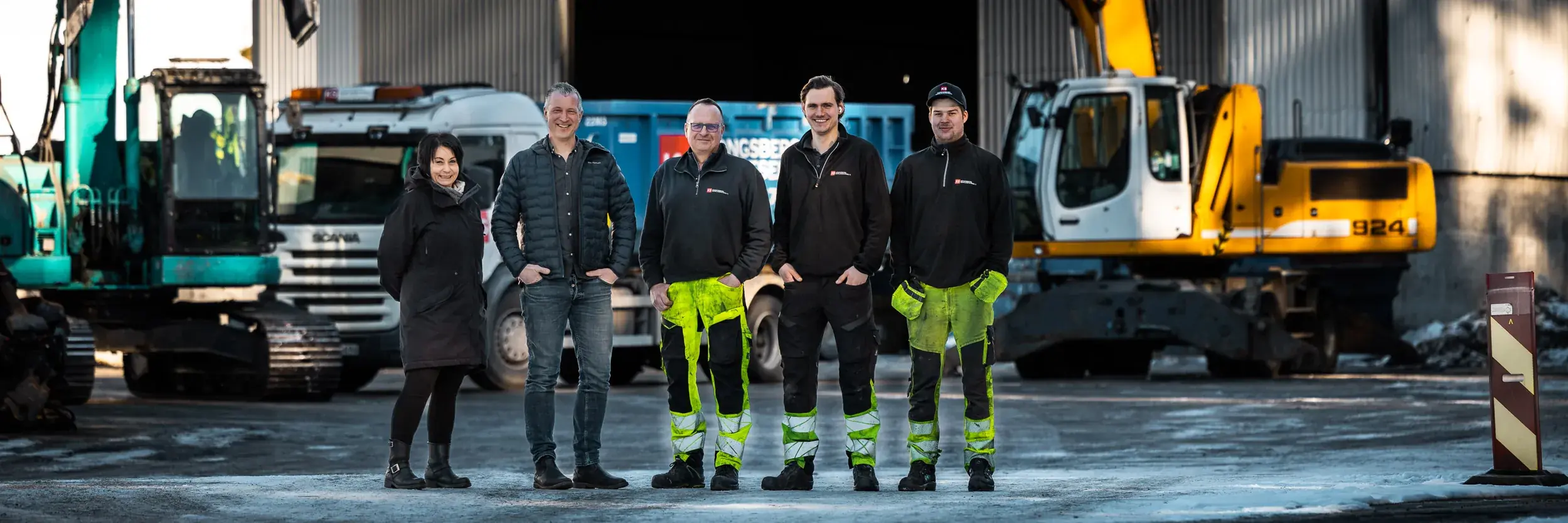 Fem ansatte hos Kongsberg Samlesentral foran gravemaskiner, lastebil og container på anlegget på Moane