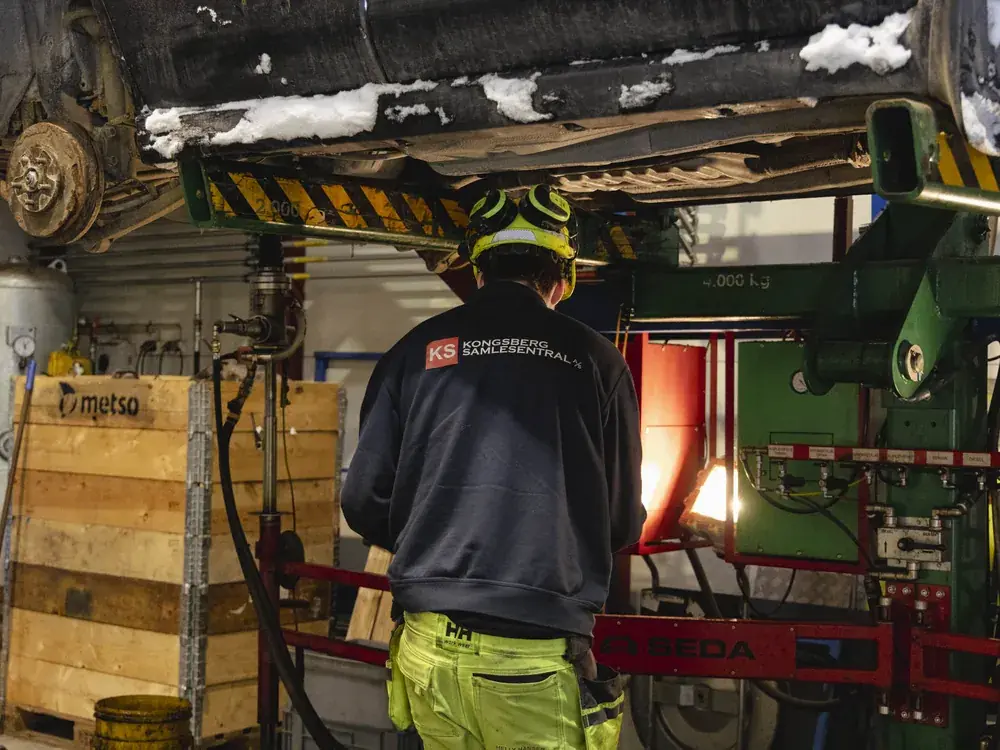 Ansatt i arbeidstøy med KS-logo i verkstedet under en løftet bil